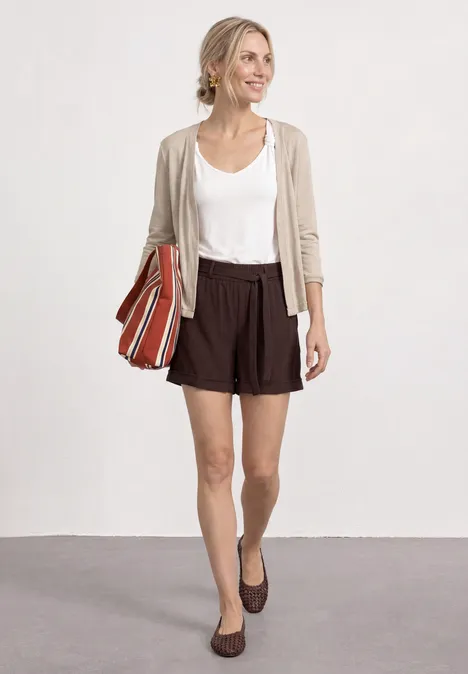 3/4-Arm Jacke in offener Passform clay sand Frau mit weißem Shirt, beiger Jacke, braunen Shorts und Loafers, mit gestreifter Umhängetasche.