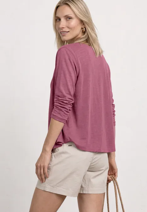 Frau von hinten in rosa Langarmshirt und beigen Shorts, die eine Tasche hält.