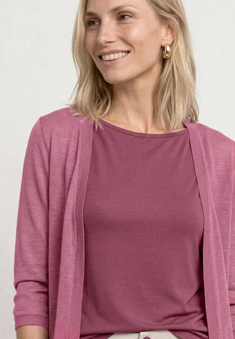 Blonde Frau lächelt und trägt ein rosa Oberteil und einen Cardigan.