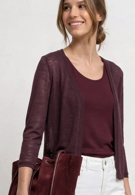 3/4-Arm Jacke in offener Passform rustic rouge Frau in weißer Hose, bordeauxrotem Top und Cardigan, hält eine passende rote Tasche.