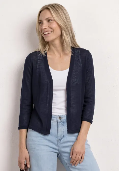 Vrouw in donkerblauwe blazer op een wit topje met lichtblauwe jeans voor een lichte achtergrond.