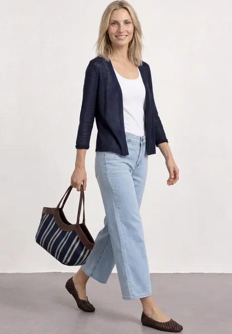Vrouw in jeans, t-shirt en blazer met tas, voor een neutrale achtergrond.
