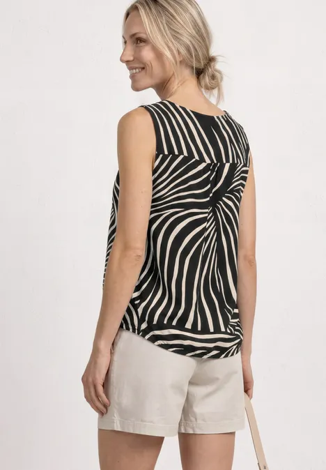 Top met V-hals en elastische zoom Black Vrouw van achter in zwart-wit gestreept top met knoop en lichte shorts, tas over de schouder.
