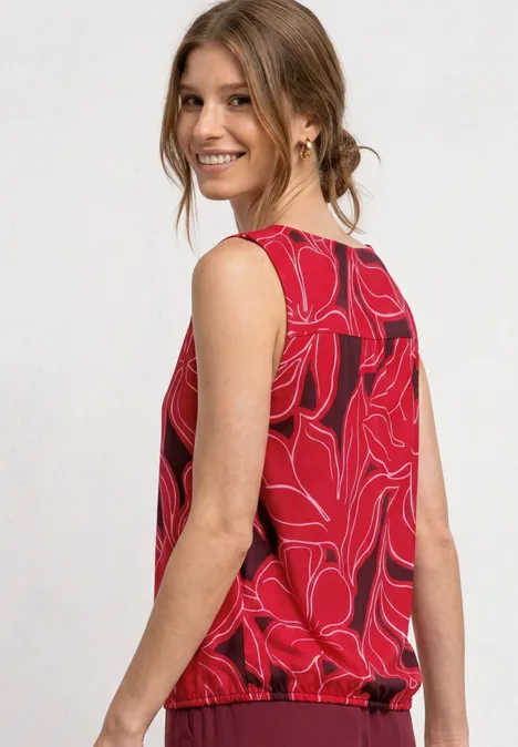 Vrouw in rood mouwloos top met abstract lijnpatroon, gefotografeerd in zijaanzicht.