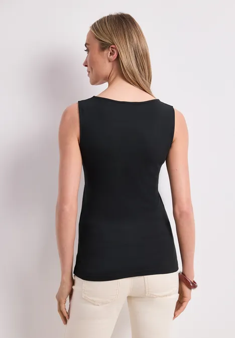 Basic Top mit Herzausschnitt Black Eine Frau steht vor neutralem Hintergrund, trägt ein schwarzes ärmelloses Top und helle Hosen, Rückansicht.