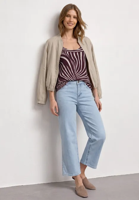 Top mit V-Neck und Deko-Detail rustic rouge Eine Frau in gestreiftem Top, heller Jacke und weiten Jeans posiert vor neutraler Wand.