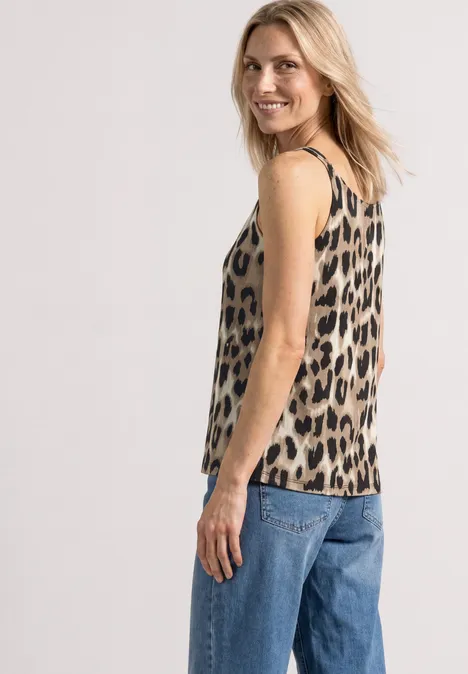 Top mit V-Neck und Deko-Detail timeless beige Frau im Profil trägt ärmelloses Leoparden-Top und blaue Jeans vor hellem Hintergrund.