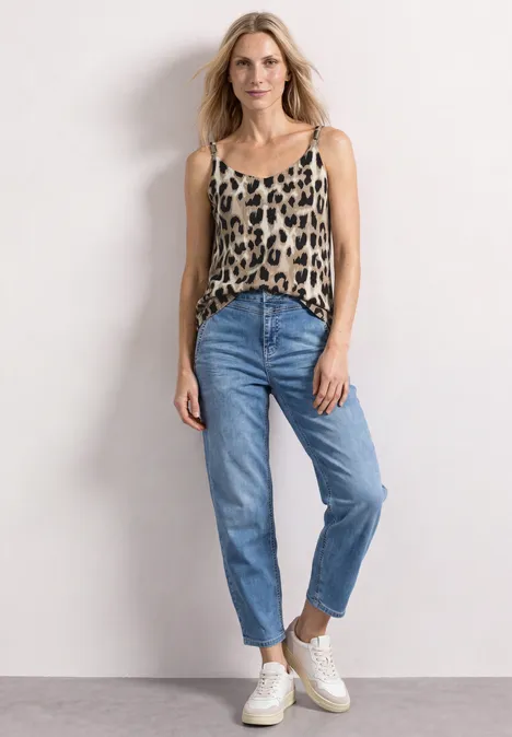 Top mit V-Neck und Deko-Detail timeless beige Frau in Leoparden-Top, blauen Jeans und weißen Sneakern steht entspannt.