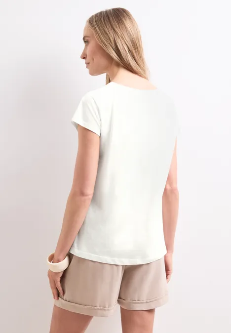 Shirt met hangende schouder en tekst off white Vrouw van achteren met een wit t-shirt en beige korte broek.