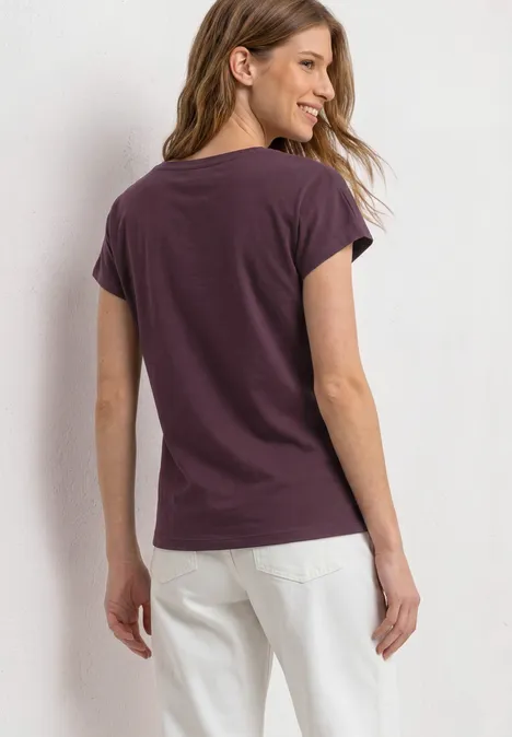 Vrouw van achteren gezien met paars T-shirt en witte broek voor heldere achtergrond.