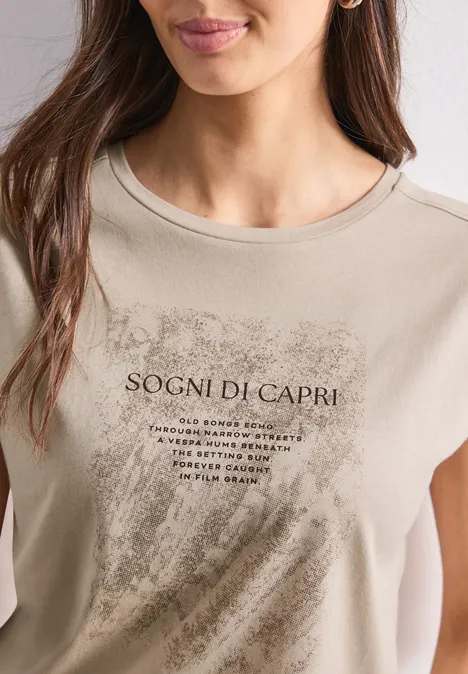 Chemise dropped shoulder avec artwork clay sand T-shirt beige porté par une femme avec l'inscription 'Sogni di Capri' et un motif de coups de pinceau.