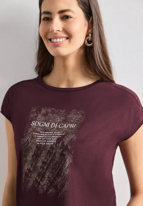 Frau trägt burgunderrotes T-Shirt mit weißem Grafikdruck und Schriftzug „SOGNI DI CAPRI“, lächelnd.
