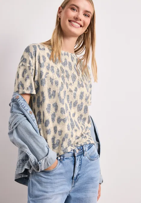 Frau im Leo-Print-Shirt und hellen Jeans, mit locker über die Schulter gehängter Jeansjacke.