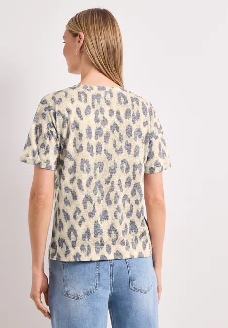 Frau von hinten in hellem Shirt mit blau-grauem Leopardenmuster und heller Jeans vor weißem Hintergrund.