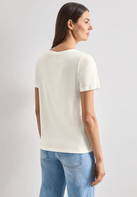 Frau von hinten in weißem T-Shirt und blauen Jeans vor weißem Hintergrund.