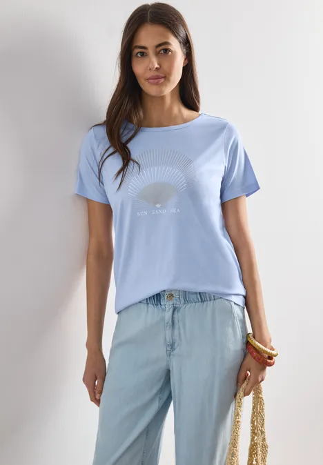 Shirt met ronde hals en foliedetails cashmere blue Vrouw met lichtblauw T-shirt, lichte jeans, houdt geweven tas vast, draagt kleurrijke armbanden.