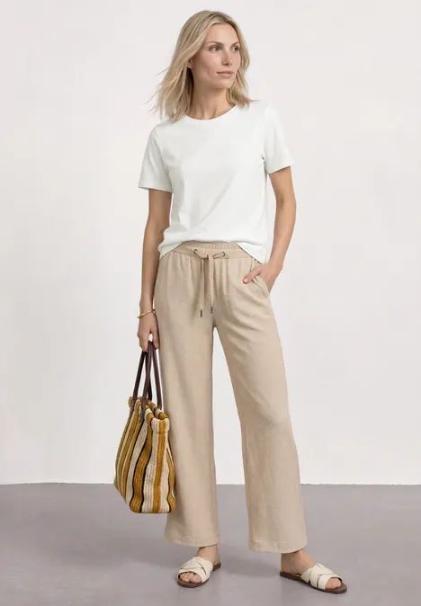 Shirt met ronde hals en geborduurd detail off white Elegante vrouw in wit T-shirt, beige broek en sandalen met gestreepte tas.