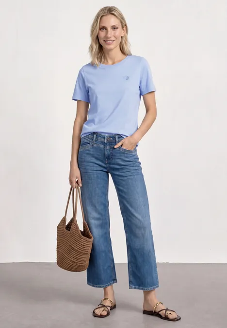 T-Shirt mit Rundhals und Embroidery Detail cashmere blue Frau in hellblauem T-Shirt, weiter Jeans, Sandalen und Korbtasche.
