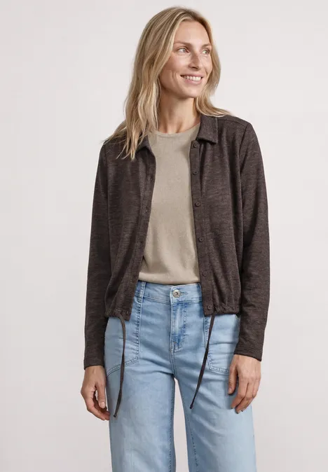 Femme portant une veste marron à carreaux, un t-shirt beige et un jean bleu sur fond blanc.