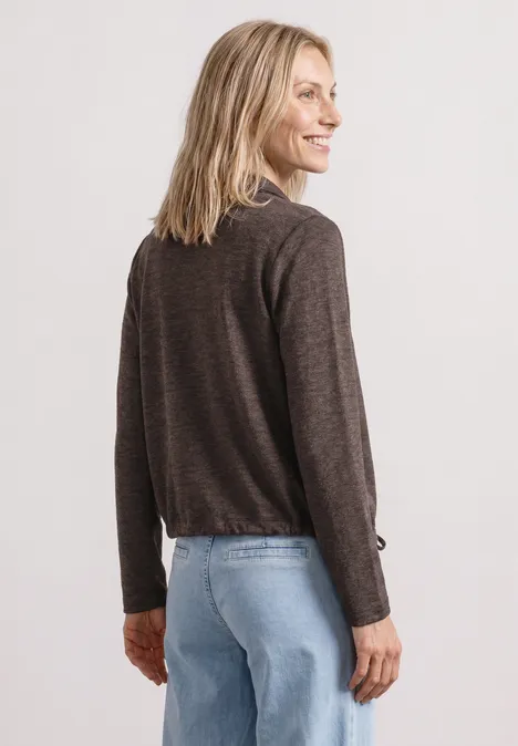 Femme de dos portant un pull marron foncé à manches longues et un jean bleu.