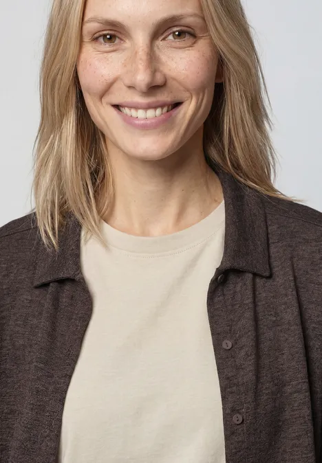 Personne aux cheveux blonds, t-shirt beige et cardigan marron sur fond neutre, visage flou.