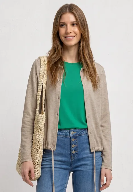 Person in beigem Cardigan, grünem Shirt, Jeans und mit Korbtasche.