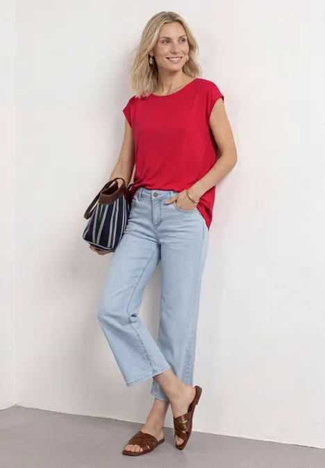 Vrouw in rood T-shirt, lichtblauwe jeans en bruine sandalen met een gestreepte handtas.