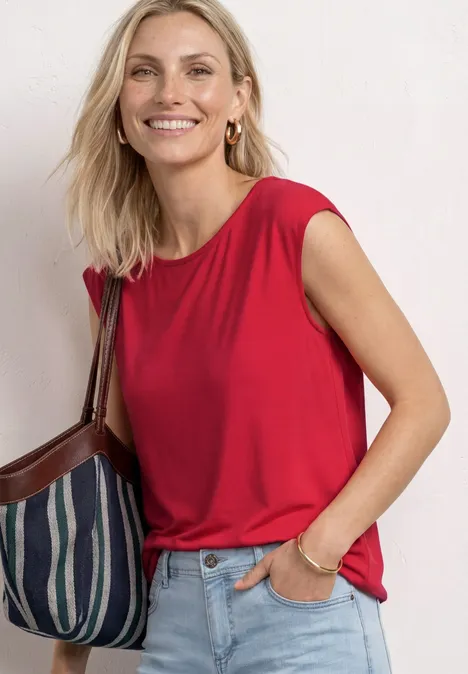 Vrouw in rood mouwloos topje, spijkerbroek en gestreepte schoudertas.