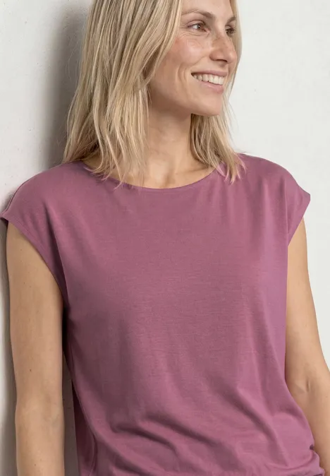 Een vrouw met halflang blond haar draagt een mouwloos, roze topje.