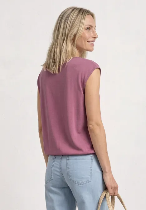Rugaanzicht van een vrouw in een roze mouwloos shirt, lichtblauwe jeans en strozak.