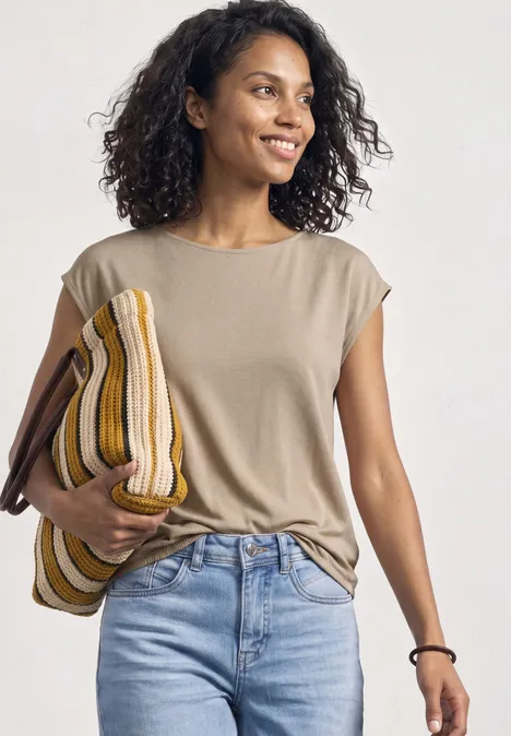 Eine Frau in beige T-Shirt und Jeans hält lässig ein gestreiftes Kissen.