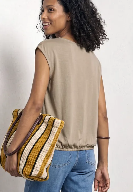 Eine Frau von hinten in beigem Top und Jeans, trägt eine gelb-weiß gestreifte Tasche.