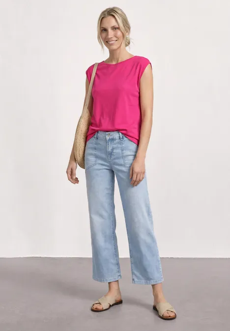 Femme en top rose, jean clair, sandales et sac beige.