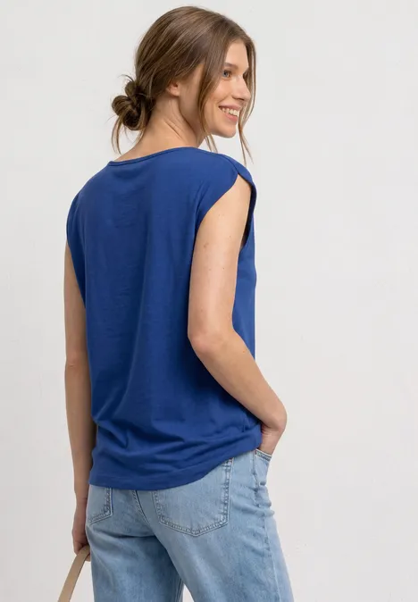 Basic shirt met boothals amparo blue Vrouw van achteren in een blauw mouwloos shirt en lichte spijkerbroek, hand in zak, haar los samengebonden.