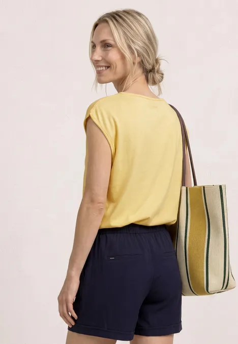 Vrouw van achteren in geel shirt, blond haar en donkere short, met gestreepte tas.