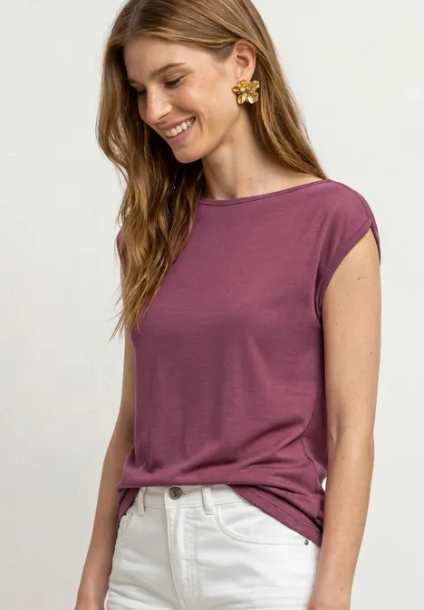 Une femme porte un t-shirt violet et un pantalon blanc.