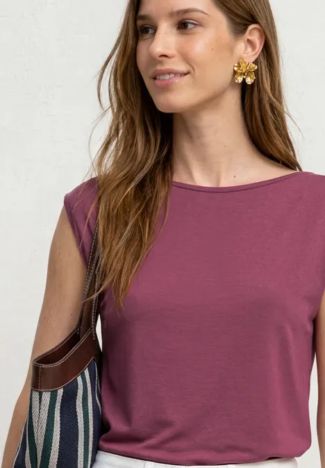 Une femme porte un haut sans manches violet, de gros boucles d’oreilles en forme de fleur et un sac rayé.