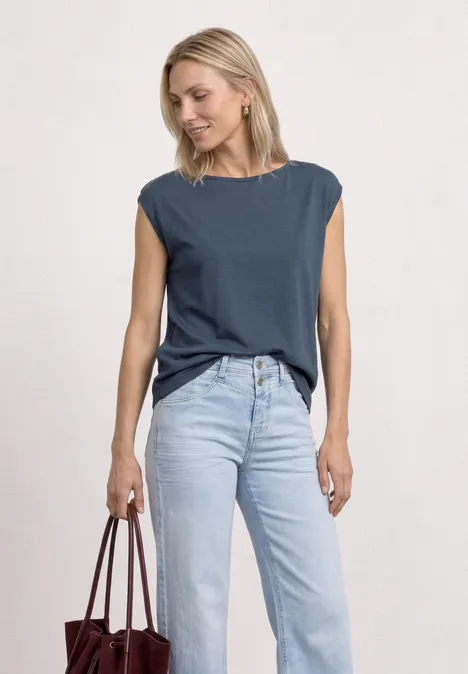 Basic shirt met boothals null Vrouw in een donkerblauwe mouwloze top en lichte jeans, met een bruine tas in haar hand.