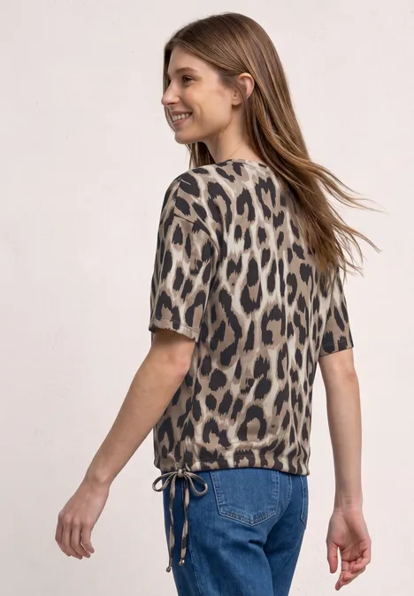 Frau in Jeans und kurzärmliger Bluse im Leopardenprint, Aufnahme in ¾-Ansicht von hinten.