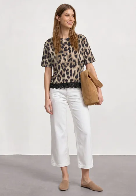 T-Shirt mit Rundhals und Spitze timeless beige Frau in Leoparden-T-Shirt, weißer Culotte, beigen Slippern und passender Tasche vor neutralem Hintergrund.