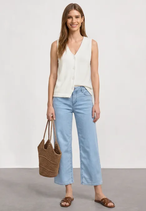 Weste in Feinstrick-Optik mit V-Neck off white Frau in weißer ärmelloser Bluse, weitem hellblauem Jeans, braunen Sandalen und geflochtener Tasche.
