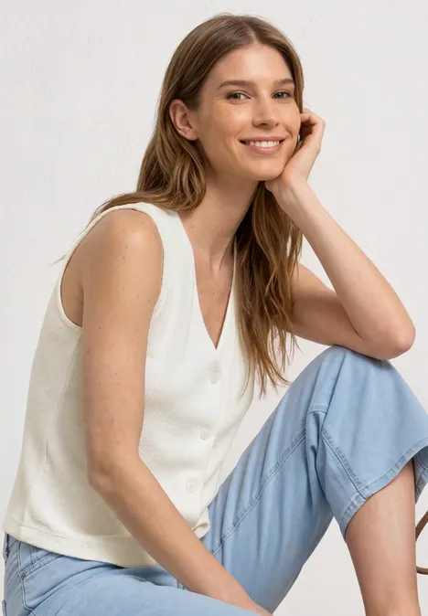 Weste in Feinstrick-Optik mit V-Neck off white Eine Frau sitzt entspannt, trägt weiße ärmellose Bluse und hellblaue 7/8-Hose.