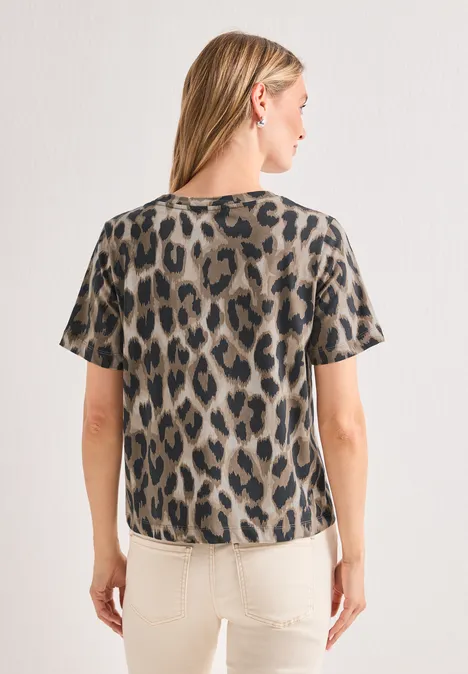 Frau von hinten in kurzärmligem Leo-Shirt und hellen Hosen vor weißer Wand.