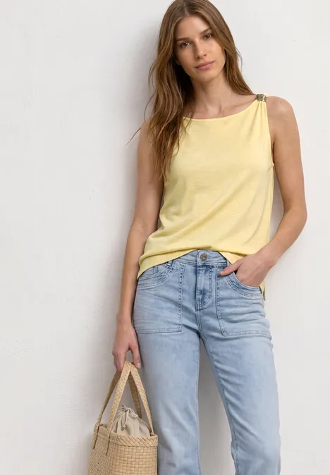 Top mit U-Boot-Ausschnitt und Schulterdetail soft yellow Frau vor neutralem Hintergrund trägt gelbes Top, blaue Jeans und hält Tasche.