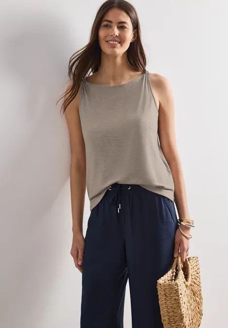 Frau in grauem Top und dunkelblauer Hose hält eine geflochtene Strohtasche.