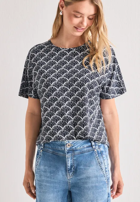 Frau trägt dunkelblaues T-Shirt mit weißem Wellenmuster und blaue Jeans