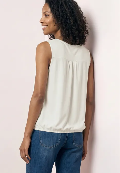 Vrouw van achteren in een witte mouwloze top en blauwe spijkerbroek voor een lichtroze muur.
