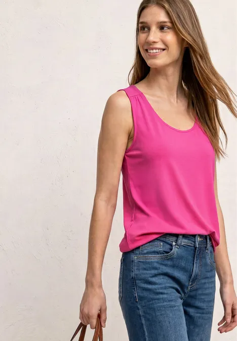 Une personne porte un haut sans manches rose et un jean bleu, tient un sac