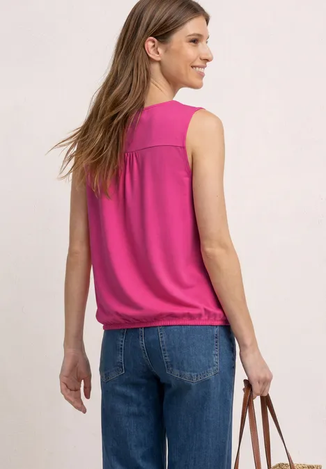 Femme de dos en top rose sans manches, jean et sac marron devant un fond clair.