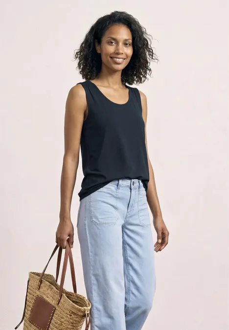 Top aus Jersey mit Elastiksaum shadowed navy Frau mit schwarzem Top, hellblauen Jeans und geflochtener Tasche vor hellem Hintergrund.